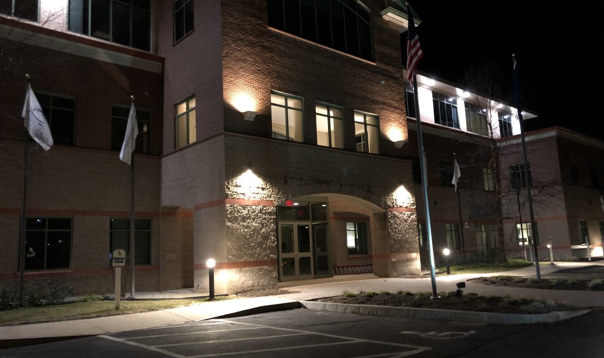 Entrance of the office building at 100 International Drive at night, with wall-mounted lights grazing the masonry, Pease Tradeport, Portsmouth, NH
