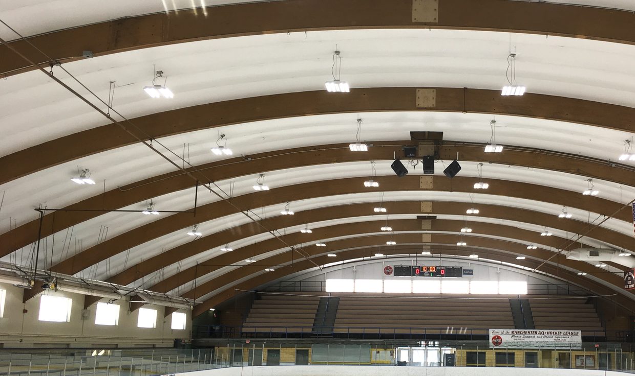 JFK Coliseum rink under LED fixtures hung between arched wood beams, Manchester, NH