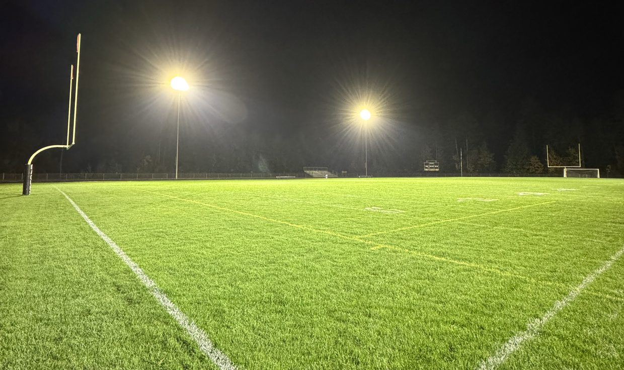 Ground-level view of the lit Kennett High School field and its LED light poles at night, Conway, NH