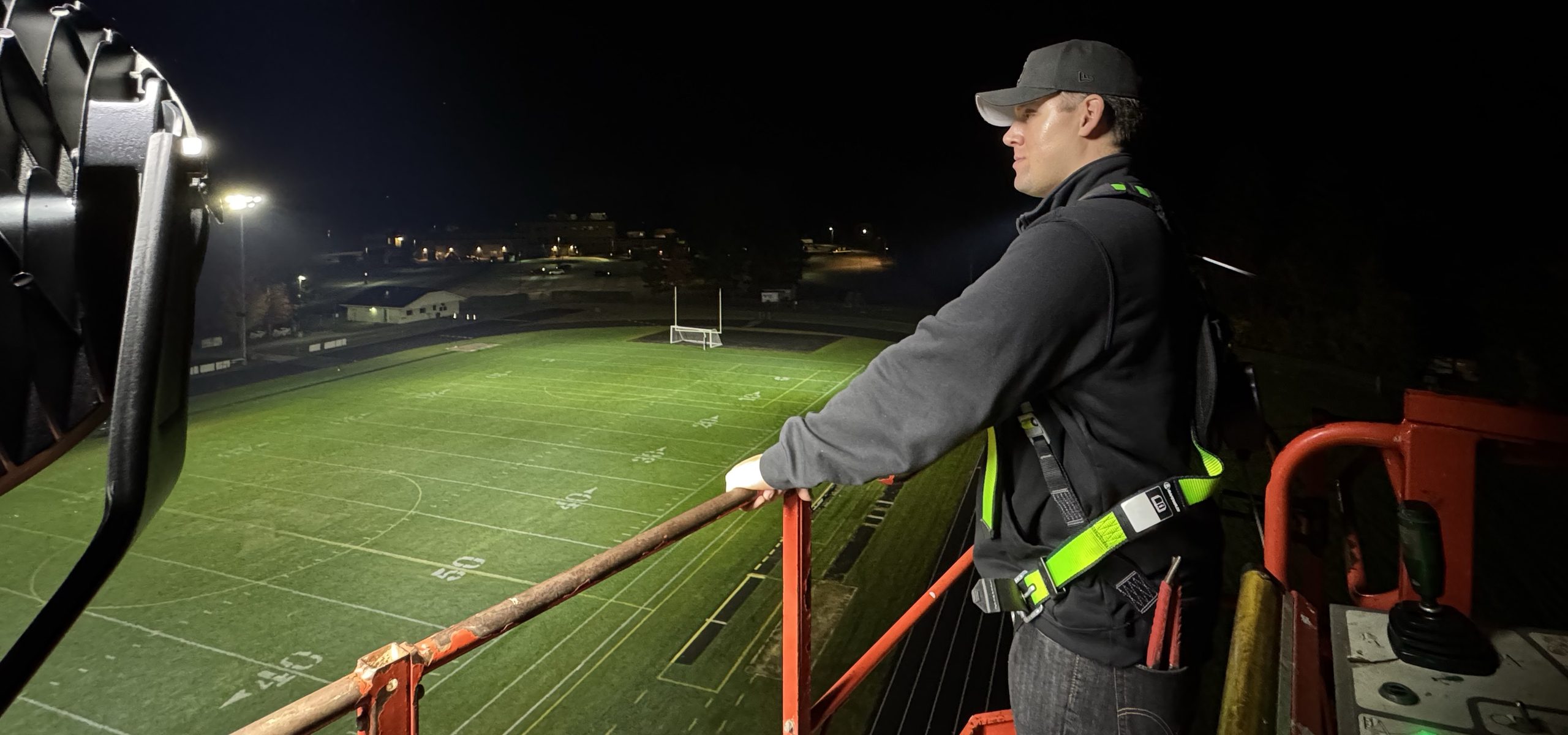 Affinity's Xavier Ocadiz on a boom lift beside a floodlight above the lit Kennett High School field at night, Conway, NH