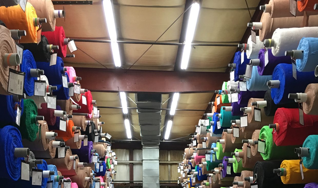 Storage aisle of colorful material rolls on racks under linear LED fixtures at Milliken Healthcare, Salisbury, MA