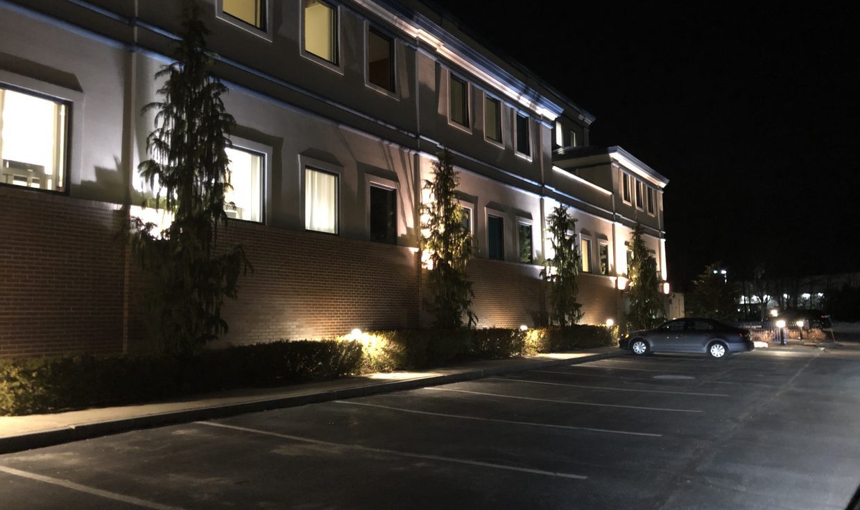Office building at One New Hampshire Avenue at night with uplit facade and evergreens, Pease Tradeport, Portsmouth, NH