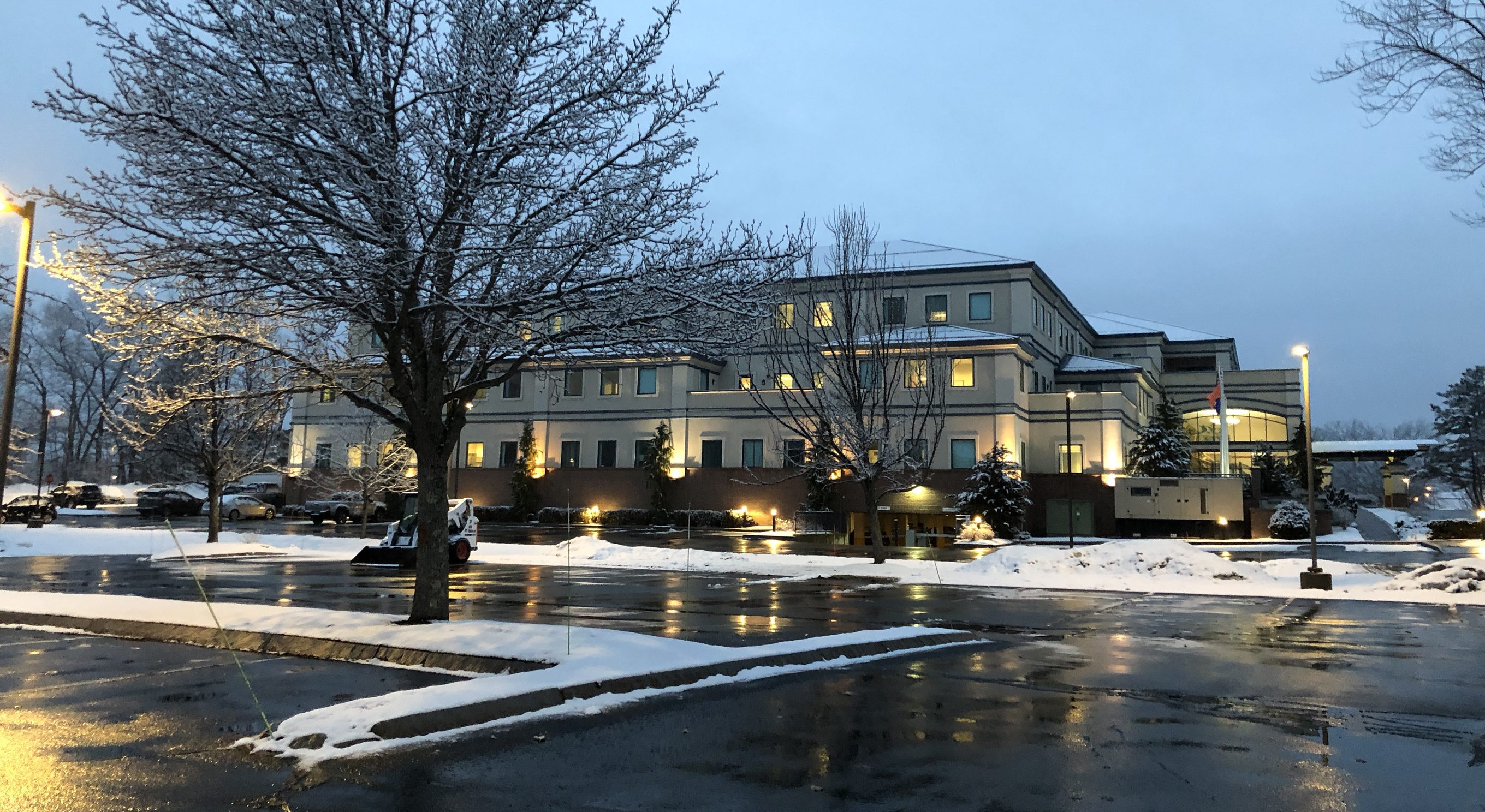 Office building at Pease Tradeport at blue hour after a snowfall, with lit windows and pole-mounted area lights, Portsmouth, NH