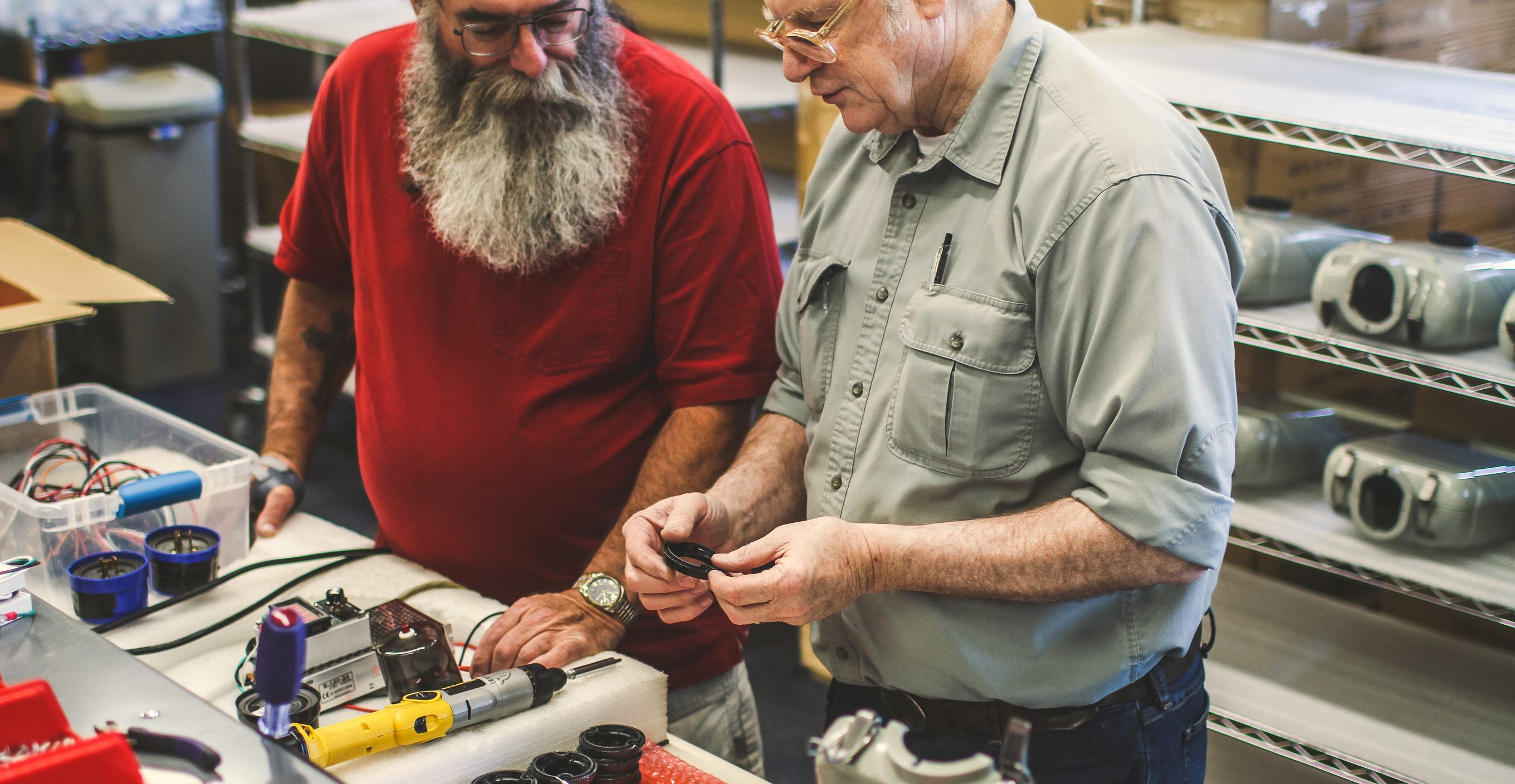 Two veteran assemblers fitting photocell receptacles at a workbench beside LED streetlight housings, Dover, NH