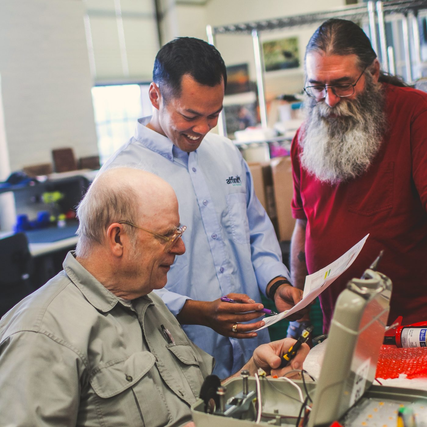 An Affinity employee reviewing paperwork with two veteran assemblers at a workbench, Dover, NH