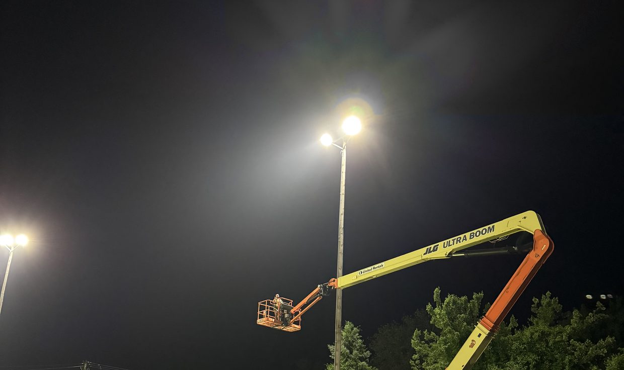 Crew member in a boom lift beside a lit LED sports-light pole at night, Veterans Memorial Park, Seabrook, NH